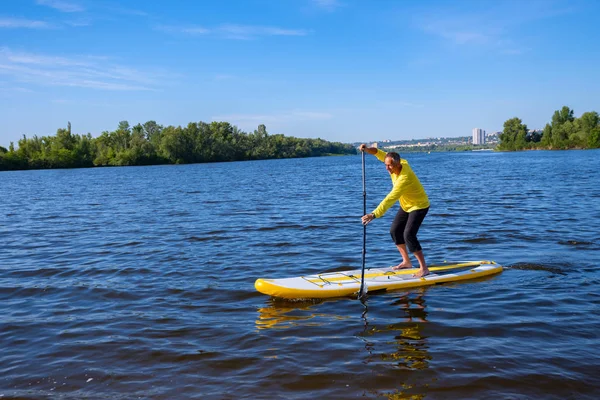 Yetişkin adam cityscape arka plan üzerinde güneşli sabahı bir Sup tahta üzerinde yelken için eğitim alıyor. Yukarı raket yatılı - stand tatil sırasında harika Aktif istirahat.