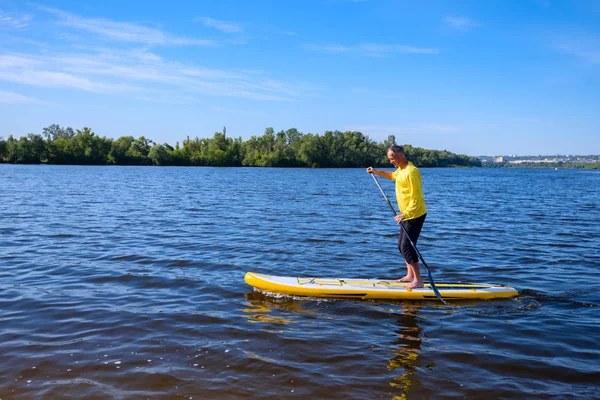 Mutlu yetişkin adam cityscape arka plan üzerinde güneşli sabahı bir Sup tahta üzerinde yelken için eğitim alıyor. Yukarı raket yatılı - stand tatil sırasında harika Aktif istirahat.