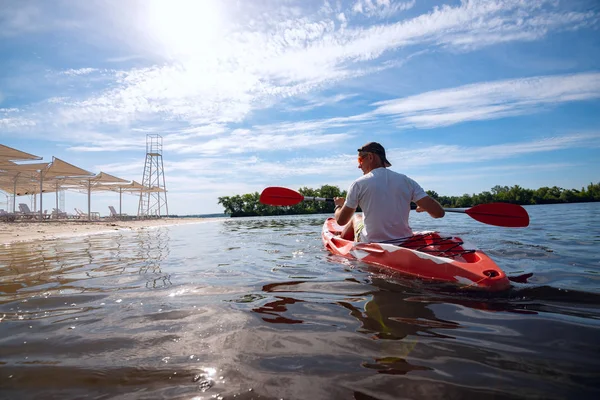 Bir güneşli sabah - su sporları tesisi üzerinde denizin plajın yanında bir kayık kürek çekmeye yetişkin adam. Arkadan görünüm, arka ışık, geniş açı.