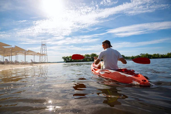 Bir güneşli sabah - su sporları tesisi üzerinde denizin plajın yanında bir kayık kürek çekmeye yetişkin adam. Arkadan görünüm, arka ışık, geniş açı.