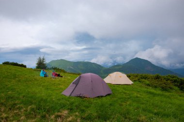 Maceracılar kahve yanındaki ağaçlık tepeler düşük ağır bulutlar altında arka planı yeşil dağ çayır üzerinde çadır dinlenme ve içki. Epik seyahat dağlarda. Geniş açı.