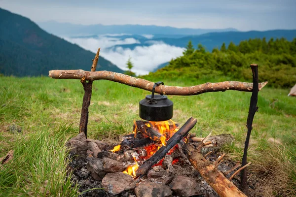 Old small kettle is heated on a bonfire on a green mountain meadow during a bad weather. Epic travel in the mountains.
