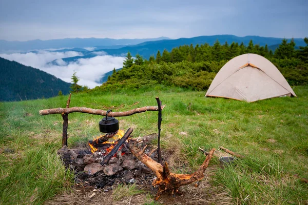 Eski küçük su ısıtıcısı bir ateşin ortasına çadır yanındaki yeşil dağ çayır üzerinde kötü havalarda ısıtılır. Dağlarda epik seyahat.