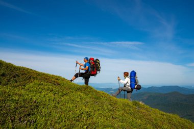 Sırt çantaları ile neşeli maceracılar yeşil dağ sırtı yürüyüş ve mavi gökyüzü arka plan üzerinde eğleniyor. Epik seyahat dağlarda. Geniş açı.