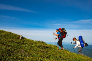 Maceracılar sırt çantaları ile yeşil dağ sırtı mavi gökyüzü arka plan üzerinde yürüyor. Epik seyahat dağlarda. Geniş açı.