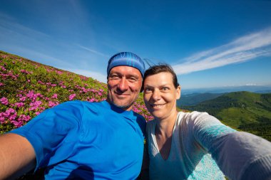 Neşeli selfie alarak ve pembe çiçekli orman gülleri arasında yeşil dağ yamacında dağlarda epik seyahat sırasında eğlenmek maceracılar birkaç.