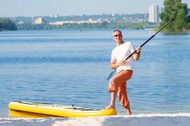 Neşeli adam Sup Kurulu yanında oynamaya cityscape arka plan üzerinde sahilde eğleniyor. Yukarı raket yatılı - stand harika Aktif istirahat.