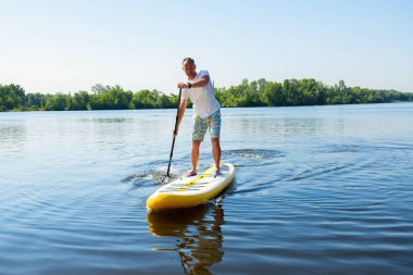 Neşeli adam bir Sup tahta büyük nehir üzerinde bir güneşli sabah yola çıkacak. Yukarı raket yatılı - stand harika Aktif istirahat. 