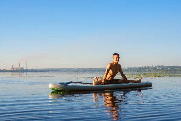 大きな川で日の出の間にSupボードでヨガを練習してる男 パドルボードの上に立つ 自然の中で素晴らしいアクティブなレクリエーション — ストック写真