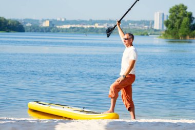 Neşeli adam kollarını açarak Sup kurulu cityscape arka plan üzerinde sahilde yanında duruyor. Yukarı raket yatılı - stand harika etkin açık rekreasyon.