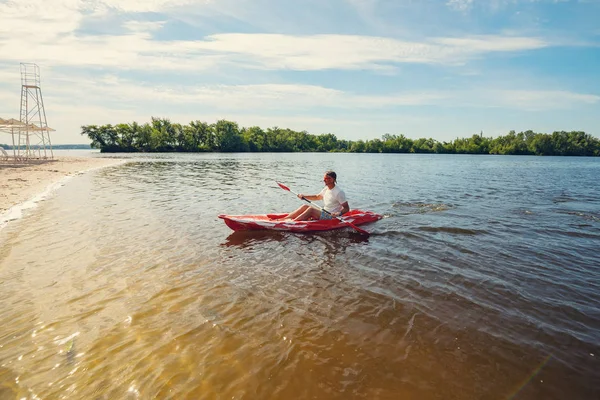 Man paddling a kayak in the sea next to the beach on a sunny morning - water sports on the resort. Wide angle.