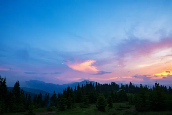 Awesome sunset in the mountains after the storm - heavy purple clouds are floating above the green wooded hills to the horizon illuminated by the rays of the setting sun.