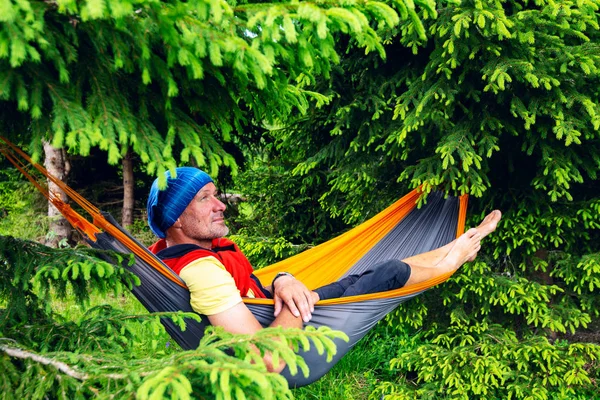 Happy adventurer relaxing in hammock on the green mountain meadow among fir trees and dreaming. Epic travel in the mountains.