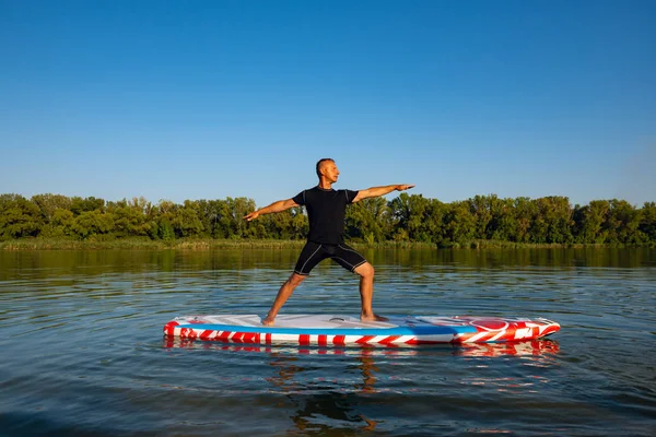 Man practicing yoga on a SUP board during sunset on a large river. Stand up paddle boarding - awesome active recreation in nature.