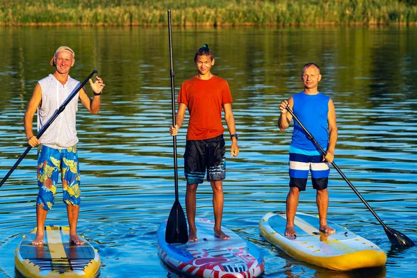 Happy friends, SUP surfers relax on the big river during sunset and enjoy life. Stand up paddle boarding - awesome active outdoor recreation.