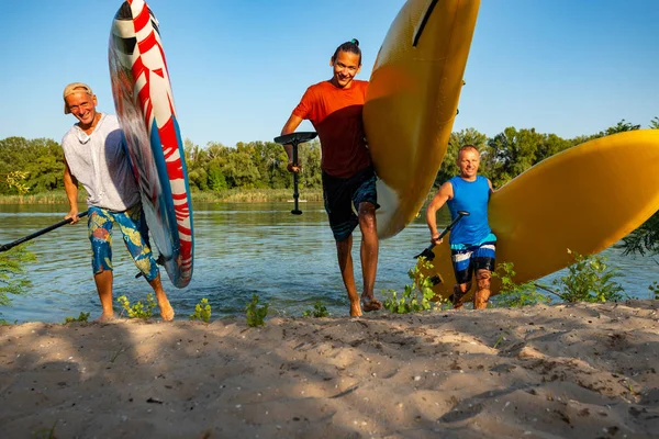 快乐的朋友们用他们手中的木板在夏天的傍晚跑出水面 玩得很开心 站起来桨登机 可怕的主动户外娱乐 — 图库照片