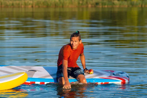 Handsome guy, teenager relaxes on SUP board and enjoy life during sunset. Stand up paddle boarding - awesome active outdoor recreation.