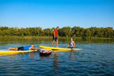 Neşeli arkadaşları, Sup sörfçü günbatımı ve having fun sırasında büyük Nehri üzerinde sakin ol. Yukarı raket yatılı - stand harika etkin açık rekreasyon. 
