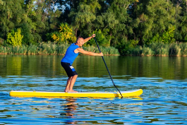 Happy man paddling on a SUP board on large river and enjoying life. Stand up paddle boarding - awesome active outdoor recreation. Side view.