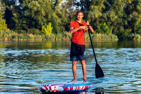 Happy guy, teenager paddling on a SUP board on large river and enjoying life. Stand up paddle boarding - awesome active outdoor recreation.