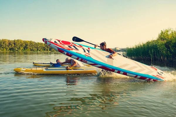 Sup のボードを手にうれしそうな友達は 夜と楽しい夏に水を実行しています スタンド アップ パドルボーディング 素晴らしいアクティブな野外レクリエーション — ストック写真