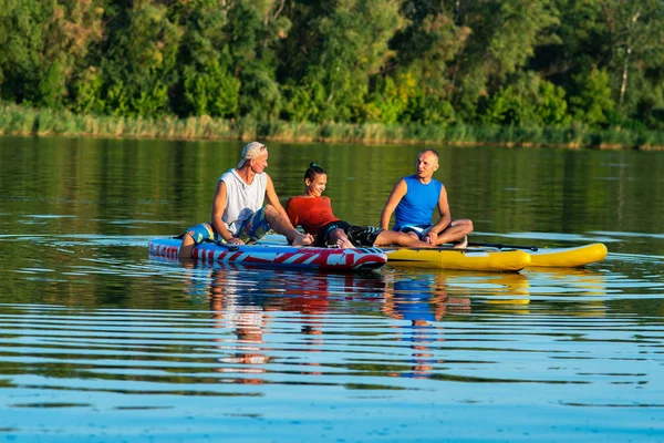 Happy friends, a SUP surfers relax on the big river during sunset, communicate and having fun. Stand up paddle boarding - awesome active outdoor recreation.