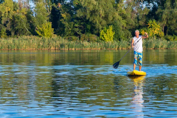 Happy man paddling on a SUP board on large river and enjoying life. Stand up paddle boarding - awesome active outdoor recreation.