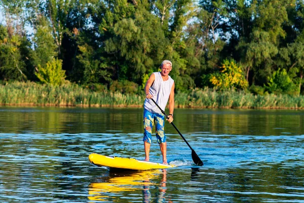 Strong man is training on a SUP board on large river and enjoying life. Stand up paddle boarding - awesome active outdoor recreation.
