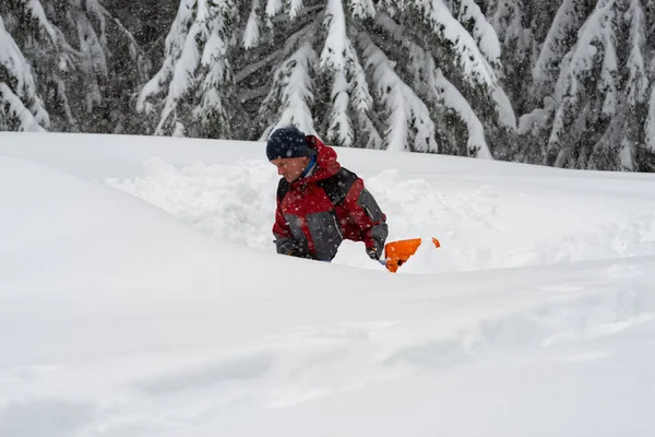 stock image Adventurer digs a cave in the snow during a snowfall - survival while traveling in winter in wilderness.