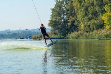 Wakeboarder arkasında sprey arasında kablo kablo parkta bir eğitim sırasında uçuyor.