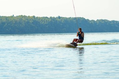Wakeboarder komik surat ile kablo Park güneşli gün eğitim sırasında hızlı sürmek.