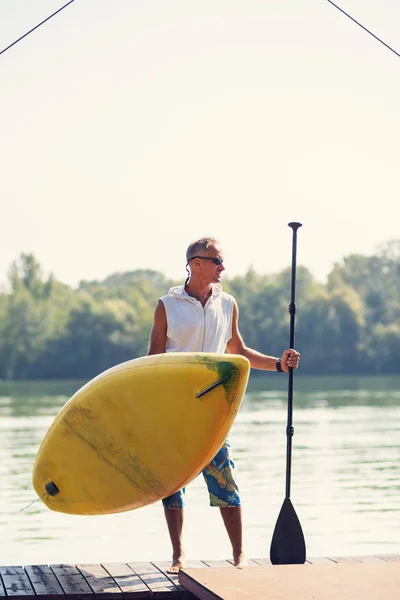 Sporty man stands on the beach with a SUP board is delighted with the sunny morning. Stand up paddle boarding - awesome active outdoor recreation.