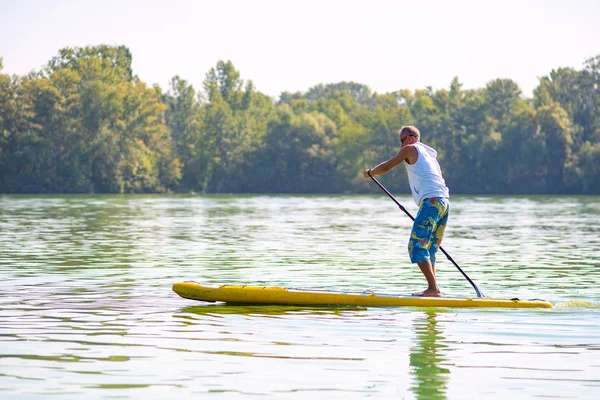 Sporty man paddling on a SUP board on large river and enjoying life. Stand up paddle boarding - awesome active outdoor recreation. Side view.