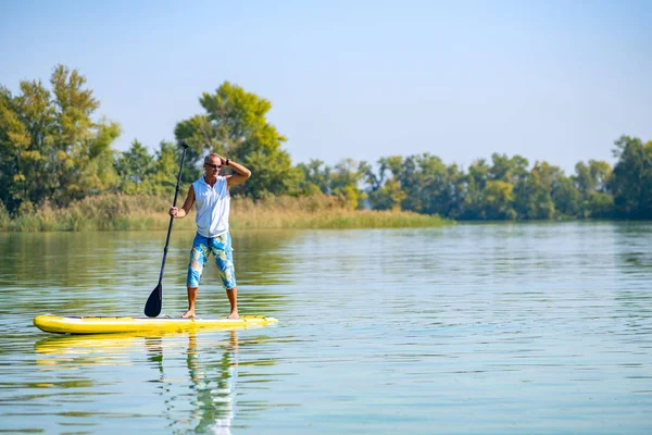 Sporty man paddling on a SUP board on large river smiling and enjoying life. Stand up paddle boarding - awesome active outdoor recreation.