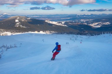 Sırt çantası ile snowboard ile ufka uzanan arka plan sıradağları üzerinde bir kar fırtınası sırasında dağ yokuş aşağı gidiyor. Geniş açı, arkadan görünüm.