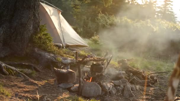 明るい朝日 見事な山の旅行の間に朝の光線でテントの横に緑の山の牧草地で焚き火の古い小さなやかんを加熱します — ストック動画
