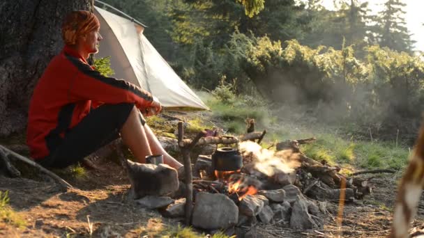 幸せな冒険家はコーヒーを飲むし 山の旅行の間に朝を見事な テントの横に緑の山の牧草地で焚き火の横にある瞑想 — ストック動画