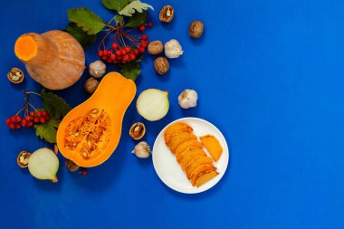 Şükran günü arka plan - pumpkins, bir tabak, soğan, sarımsak, ceviz, üvez mavi zemin üzerine kızarmış kabak dilimleri. Üstten görünüm, kopya alanı.