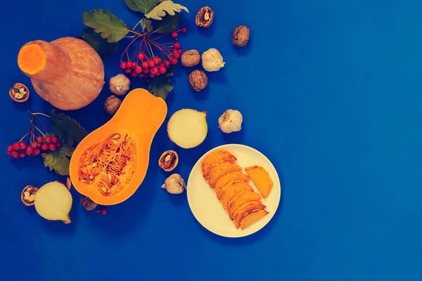 Thanksgiving  background - pumpkins, fried pumpkin slices on a plate, onions, garlic, walnuts, mountain ash on the deep blue background. Top view, copy space. Vintage image.