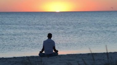Sörf, deniz üzerinde şaşırtıcı günbatımı sırasında pratik yoga yanındaki sahilde adam oturur. Arkadan görünüm.