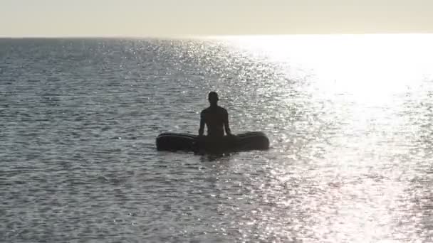 海で膨脹可能なマットレスの上の男は 晴れた夜に揺れる波にヨガの練習します バックライト付き — ストック動画