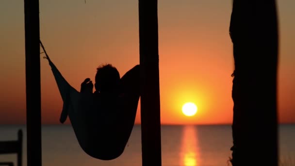 Człowiek Relaksuje Hamaku Werandzie Bungalow Podziwiając Zachód Słońca Nad Morzem — Wideo stockowe