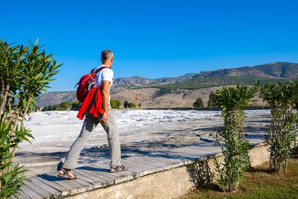 Happy traveler goes along and admires awesome view of snow-white hills and ancient ruins  - Pamukkale, Turkey tourist landmark. Back view.