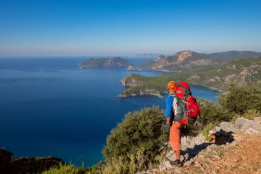 Seyahat etmek sırt çantası ile cliff üzerinde duruyor ve şaşırtıcı deniz güneşli gün defne hayran. -harika macera seyahat Türkiye'de. Arkadan görünüm, geniş açı.
