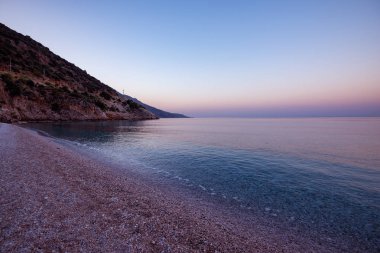 Kayalık sahilleri tarafından çevrili Akdeniz'in turkuaz suları sunrise - Ölüdeniz, Türkiye'de turist Simgesel Yapı sırasında yemyeşil çam ağaçları ile kaplı. Pembe tonlarda deniz manzarası.