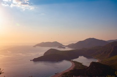 Panoramik manzaralı kayalık sahilleri günbatımı - Ölüdeniz, Türkiye'de turist Simgesel Yapı sırasında Akdeniz'in turkuaz suları ile çevrili yemyeşil çam ağaçları ile kaplı.