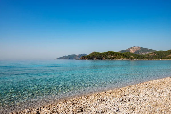 Kayalık sahilleri tarafından çevrili Akdeniz'in turkuaz suları güneşli bir günde - Ölüdeniz, Türkiye'de bir turist dönüm noktası yemyeşil çam ağaçları ile kaplı.