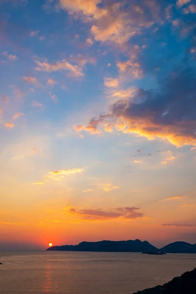 Amazing sunset over mediterranean sea near the city of Kas, Turkey - travel along Lycian way. Orange sun sets in purple sea over islands on the horizon. Wide angle, vertical image.