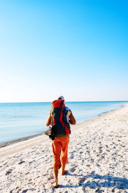 Güneşli bir günde ıssız plajda turkuaz denizin yanında seyahat etmek sırt çantası ile gider. Deniz kıyısı harika macera seyahat. Arkadan görünüm.