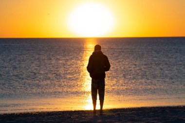 Adam sonraki sörf için sahilde standları, şaşırtıcı günbatımı denizin hayran ve derin derin düşünür. Korku veren seyahat deniz kenarına. Arkadan görünüm, arkadan.